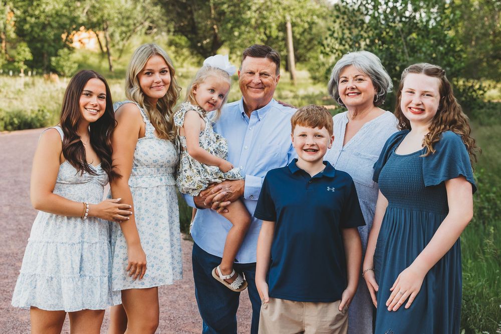 A group in coordinating blue and white outfits poses together outdoors for casual family photos in a natural setting.