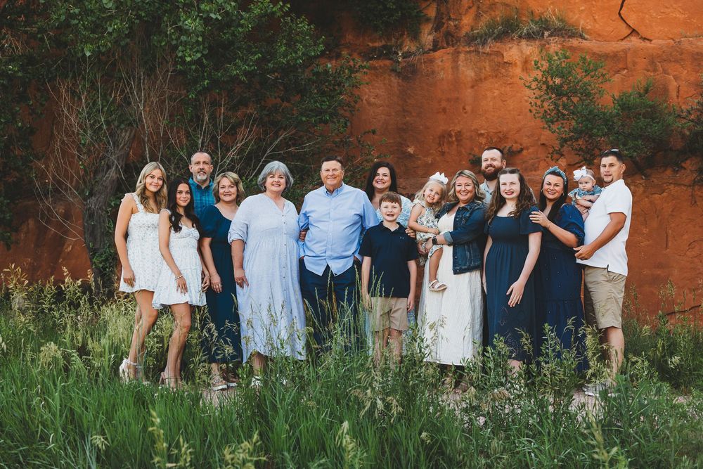 A group poses together outdoors against a striking red rock wall with green grass and foliage.