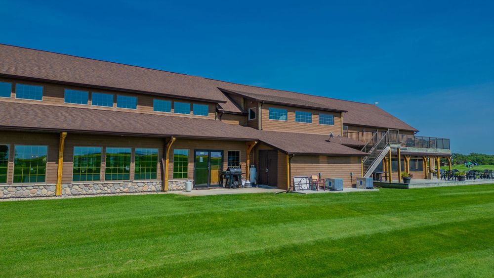 Modern rustic event venue building with wood beams and large windows overlooking manicured green lawns.