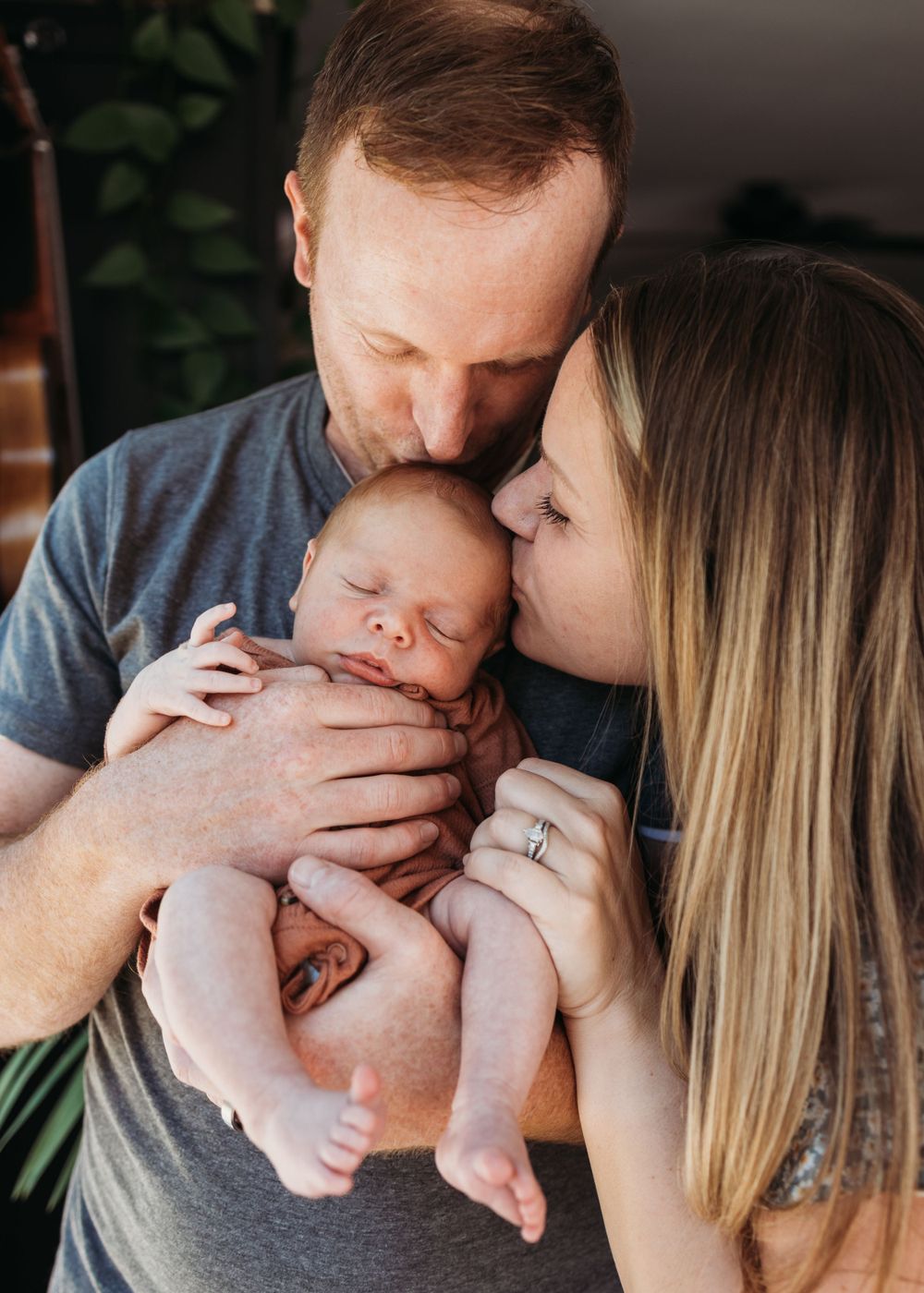 Parents share an intimate moment with their newborn baby in gentle indoor lighting.