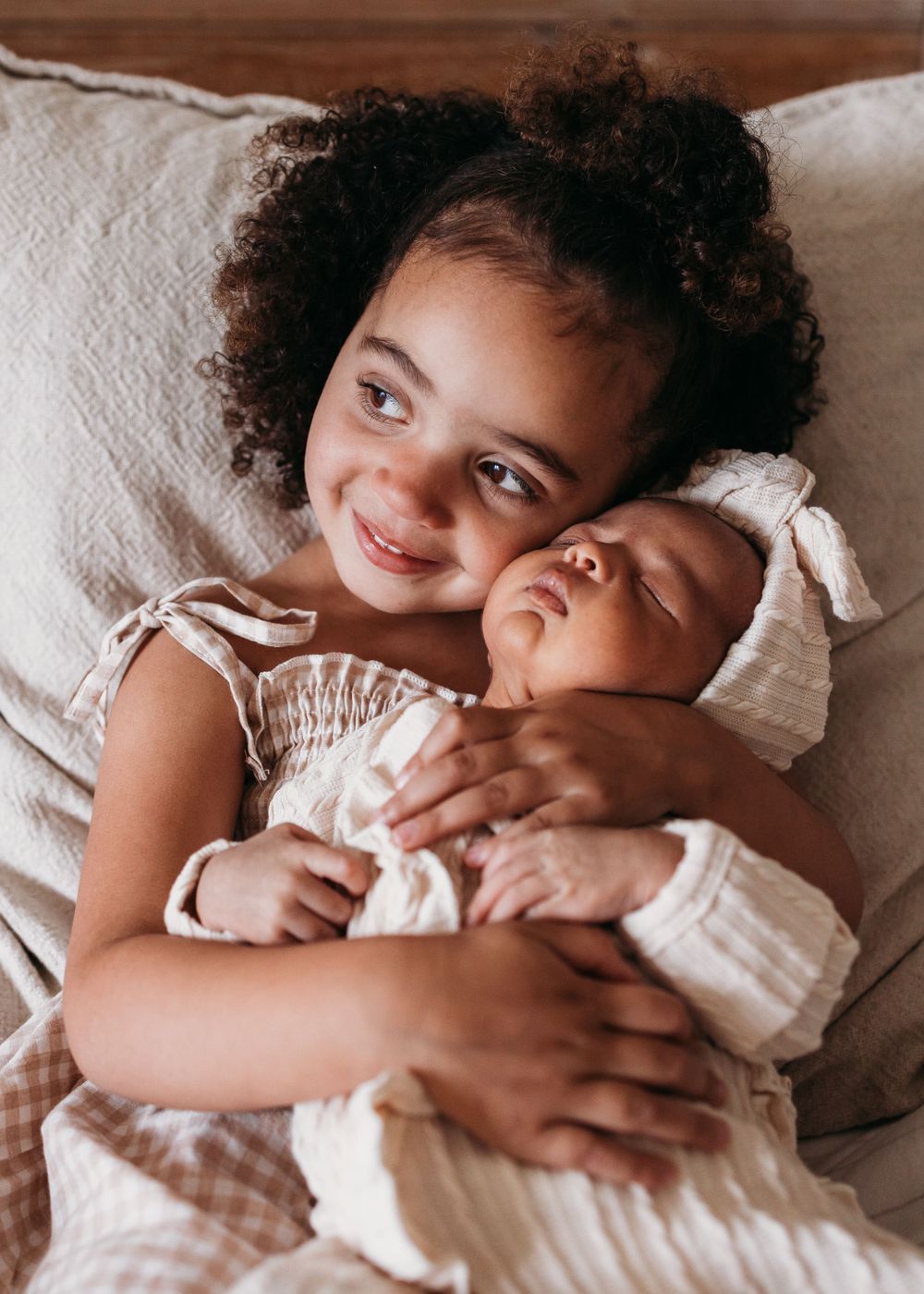 Two children share a tender moment while resting on white bedding in warm lighting.