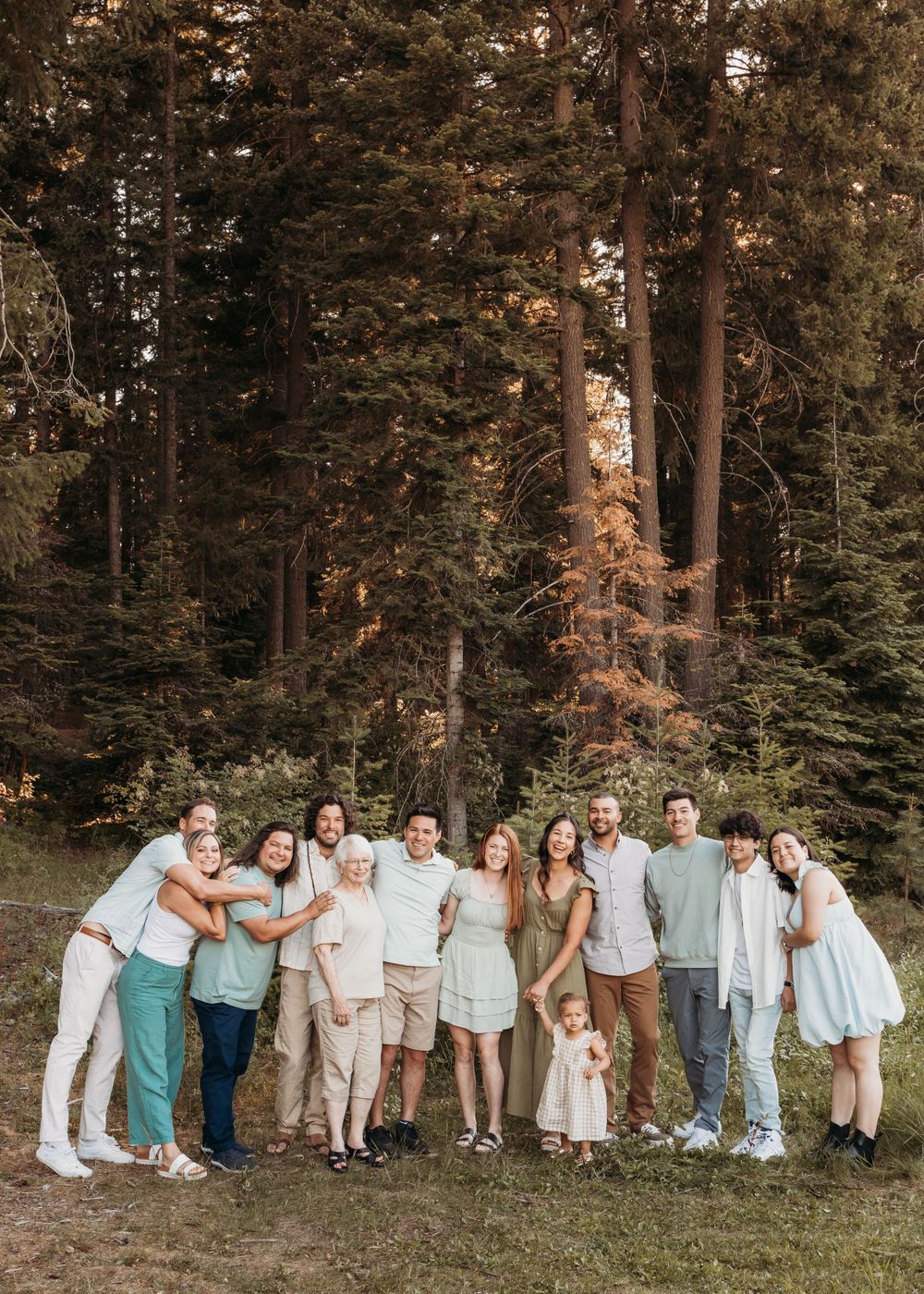 A group poses together for a photo in front of tall pine trees at sunset.