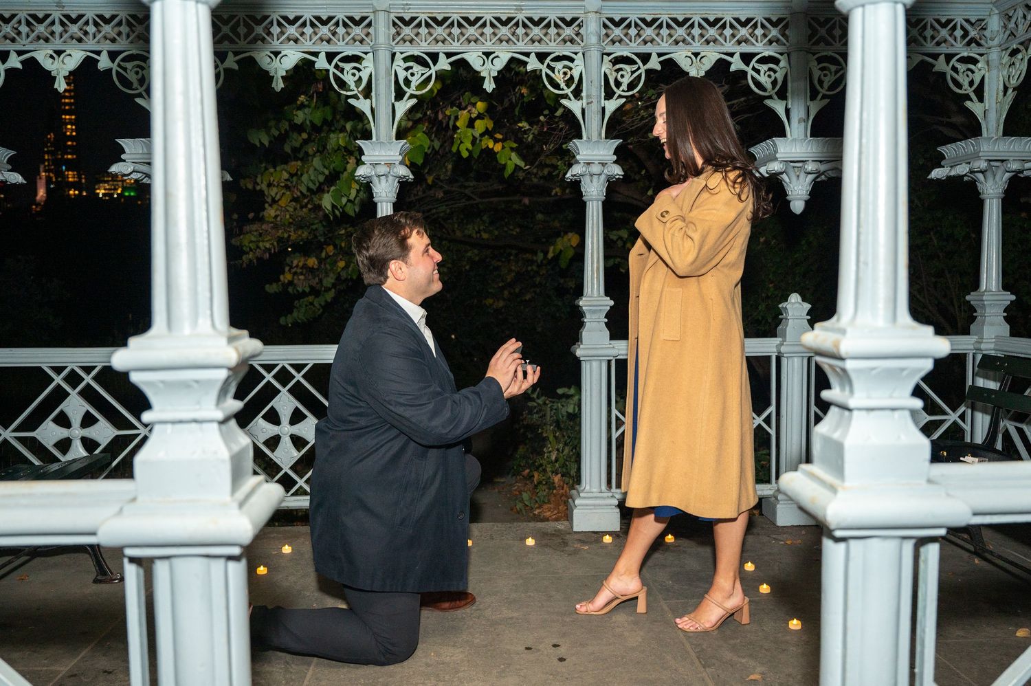A romantic marriage proposal takes place at night in a white ornate gazebo decorated with lights captured by NYC proposal photographer.