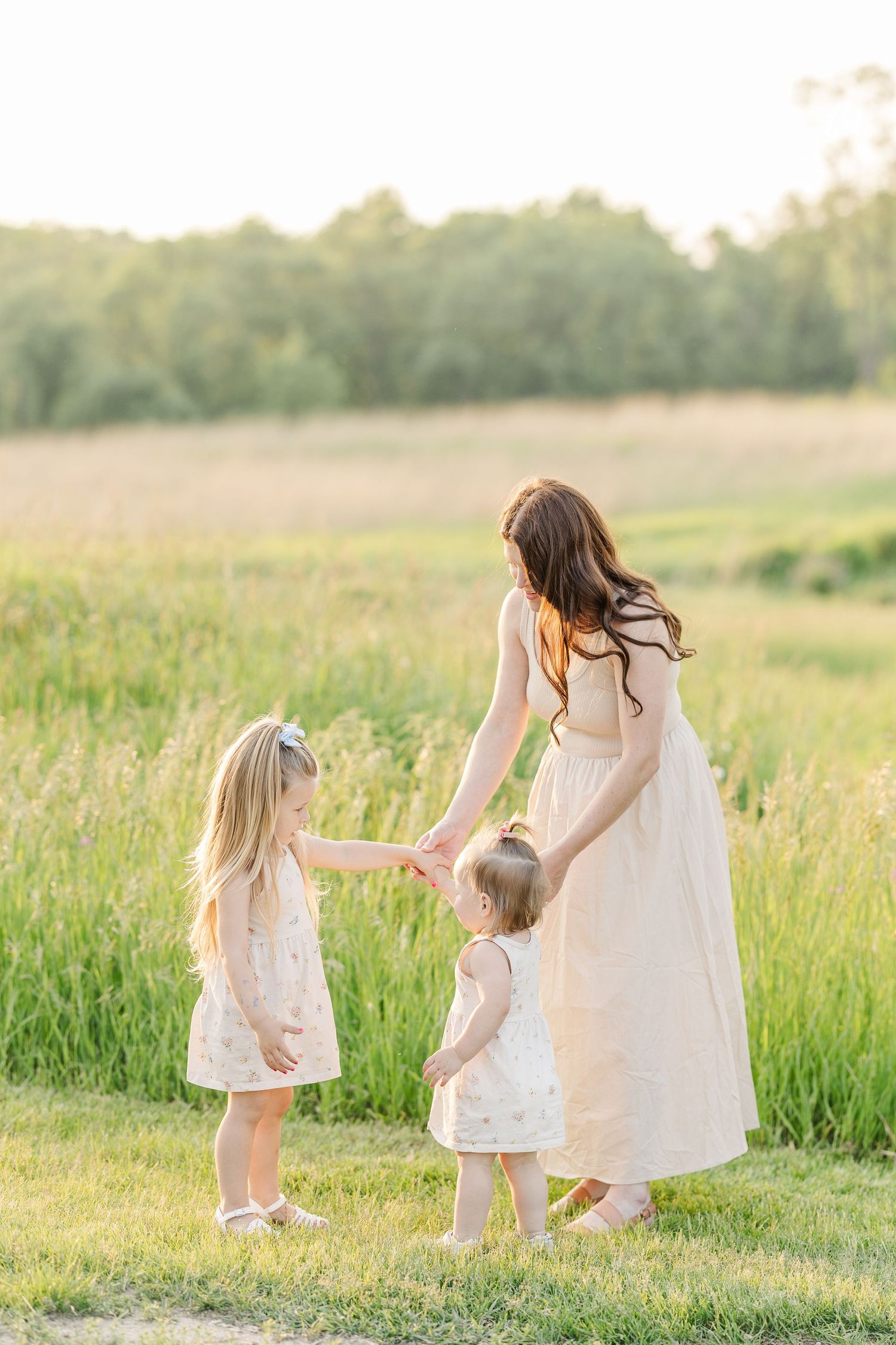 A family in white dresses holds hands while standing in a sunlit meadow during golden hour.