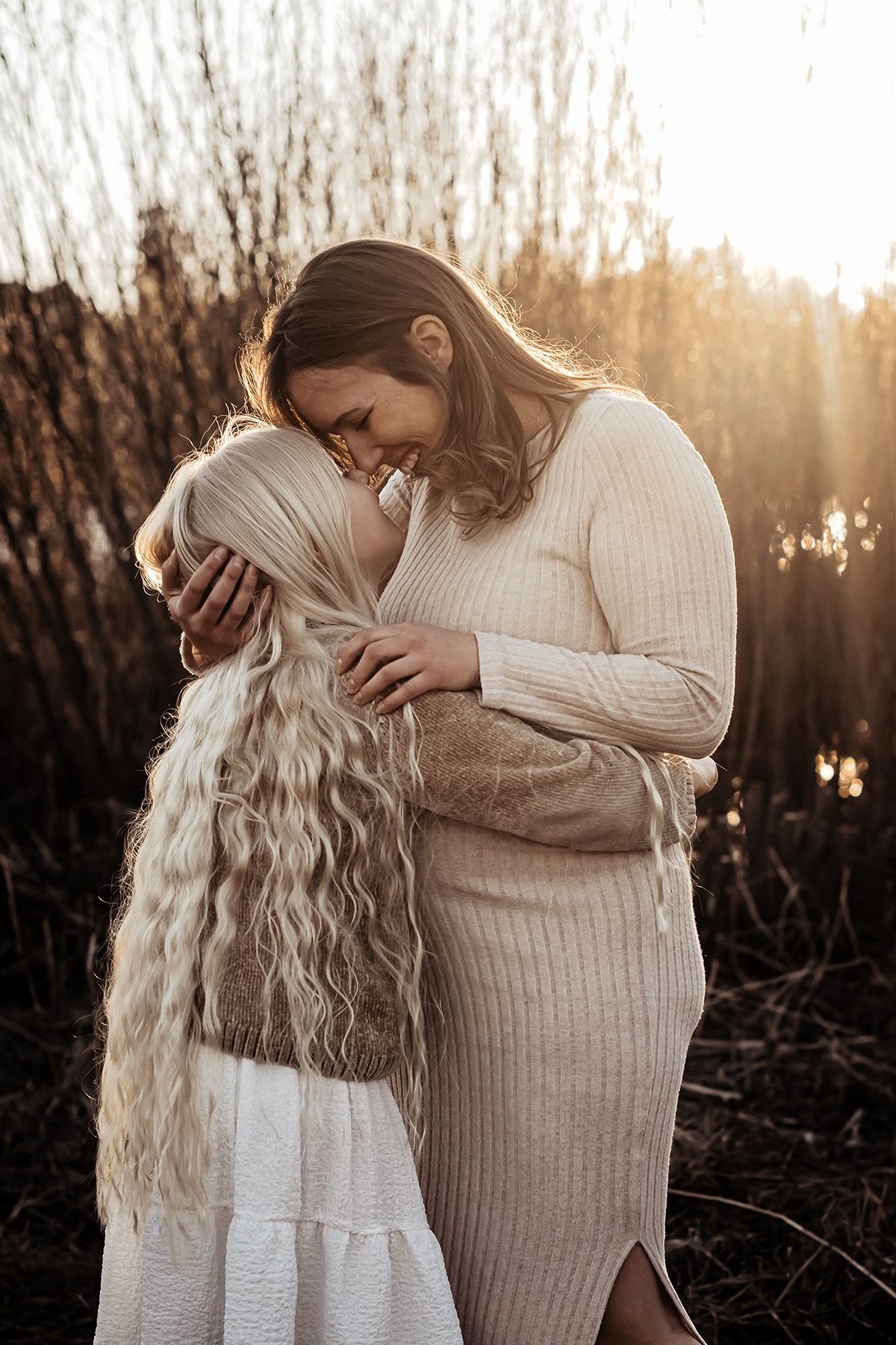 Mot och dotter kramas, dottern har långt blondt hår och mamman är gravid, gravidfoto i Finspång av Lets Bloom Media.