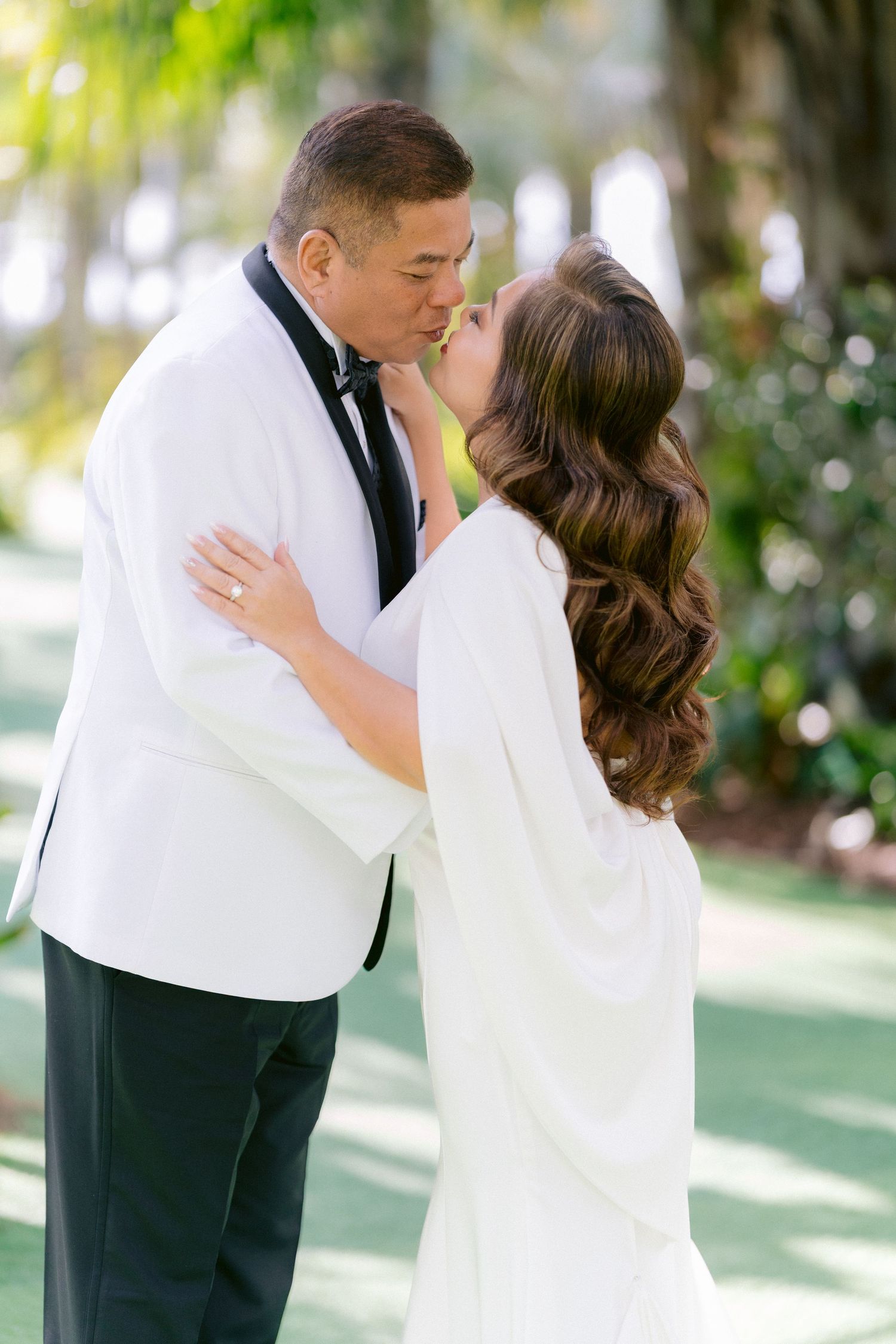 Two people share a romantic kiss at an outdoor wedding, wearing elegant white formal attire at Lake Nona Wave Hotel.