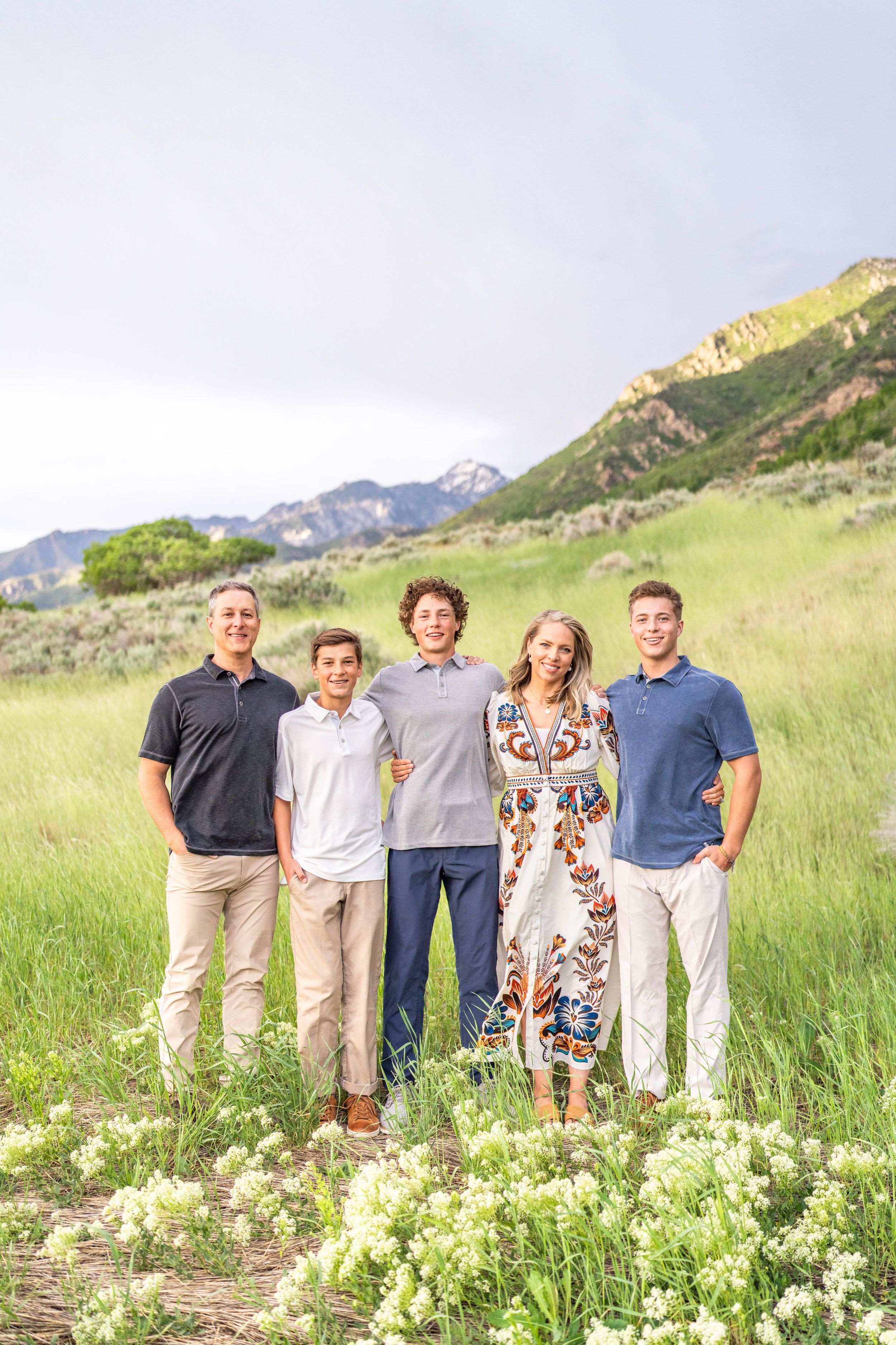 A family poses together by a wooden fence during autumn with mountains and golden foliage in the background.