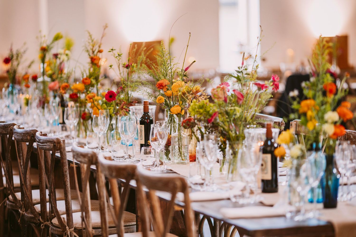 Wedding reception tables decorated with colorful wildflower centerpieces and elegant place settings in rustic venue.