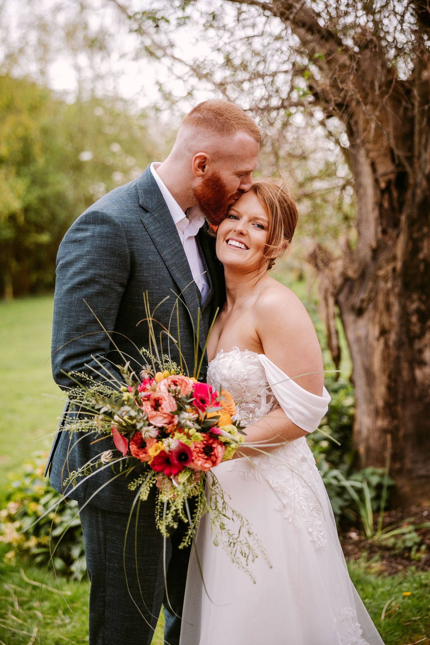 Couple embraces in an outdoor garden setting with vibrant fall-colored wedding bouquet.