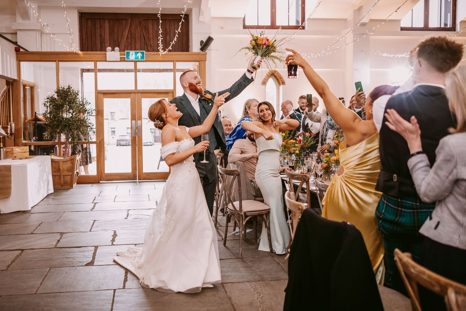 Wedding celebration at indoor reception venue with guests raising toasts and sharing joyful moments.