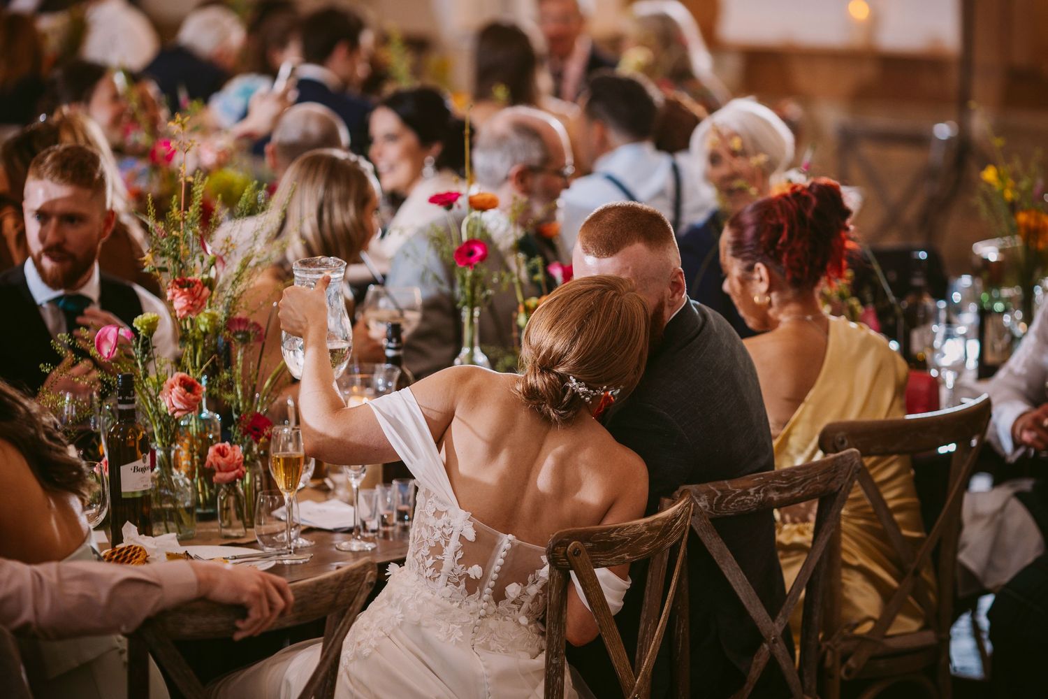 Reception guests seated at decorated tables with vibrant autumn-colored flower arrangements.