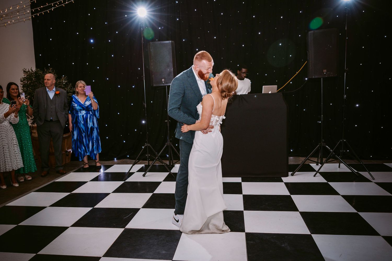 Dancers perform low dips on a black and white checkered dance floor during a reception celebration.