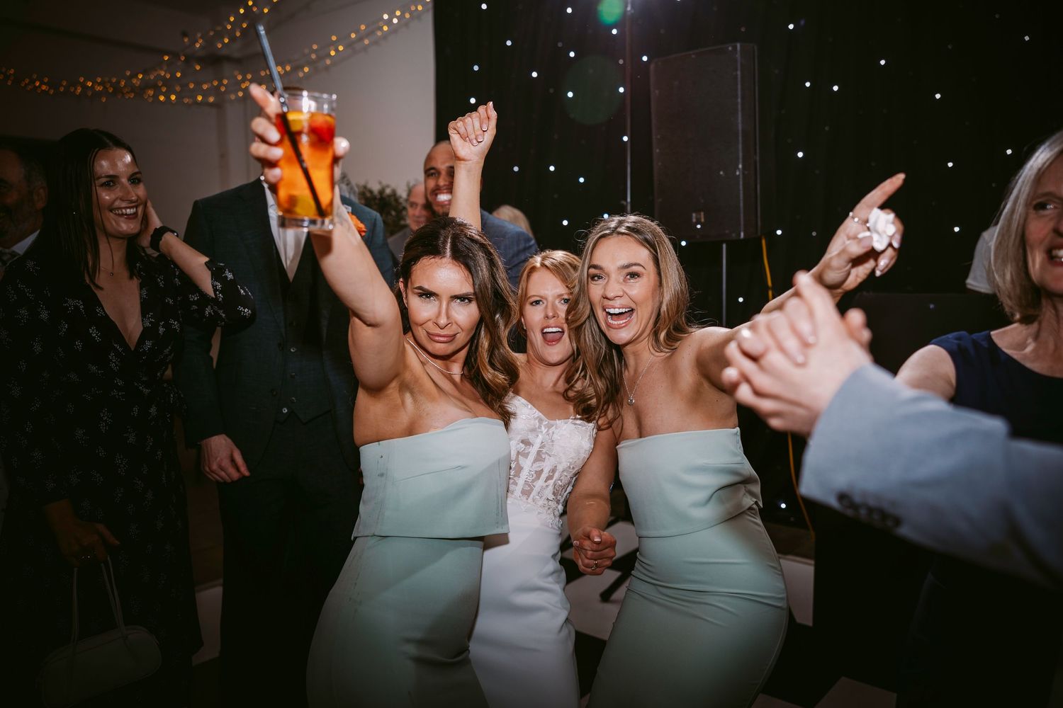 Bridesmaids in matching light blue dresses celebrating on dance floor at wedding reception.