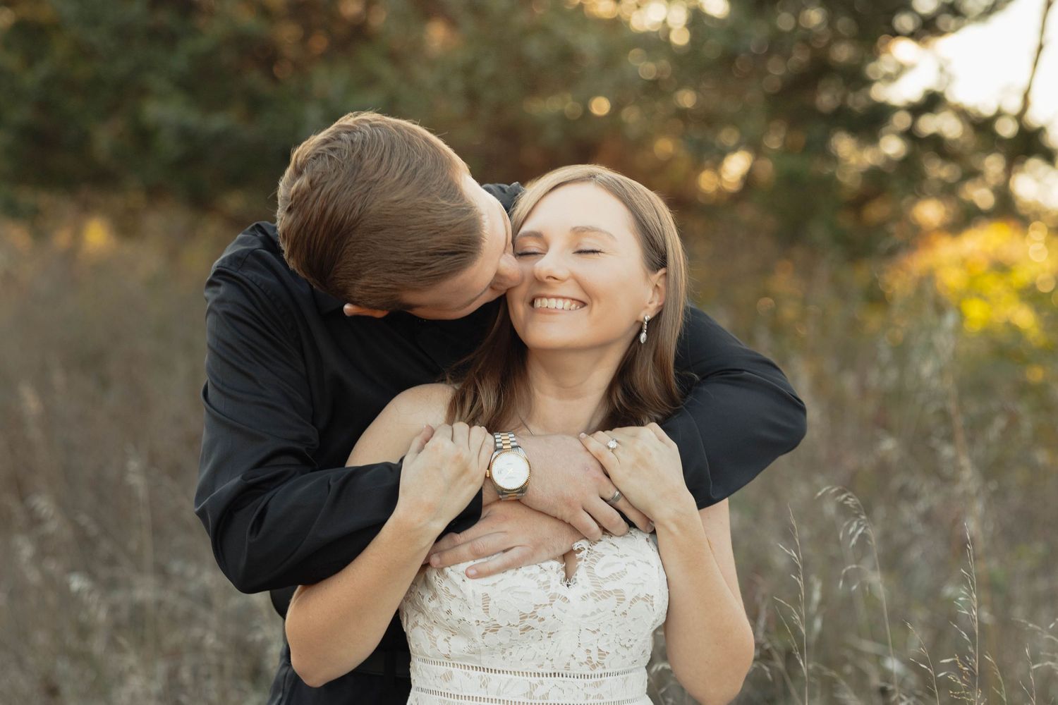 Couple embraces in golden field during sunset photoshoot wearing wedding dress and black suit.