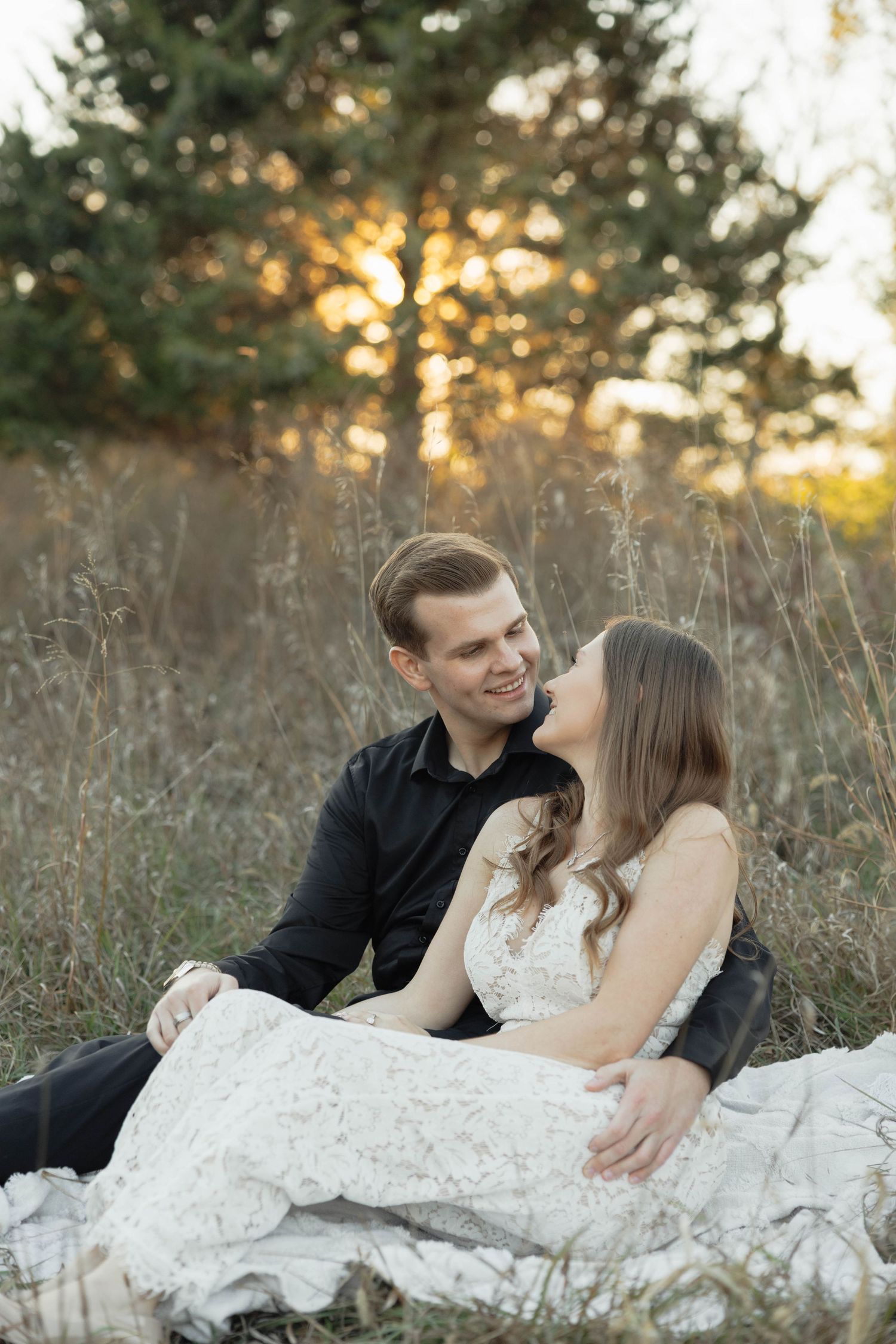 A couple enjoys a romantic moment together while laying in a rustic field during sunset.