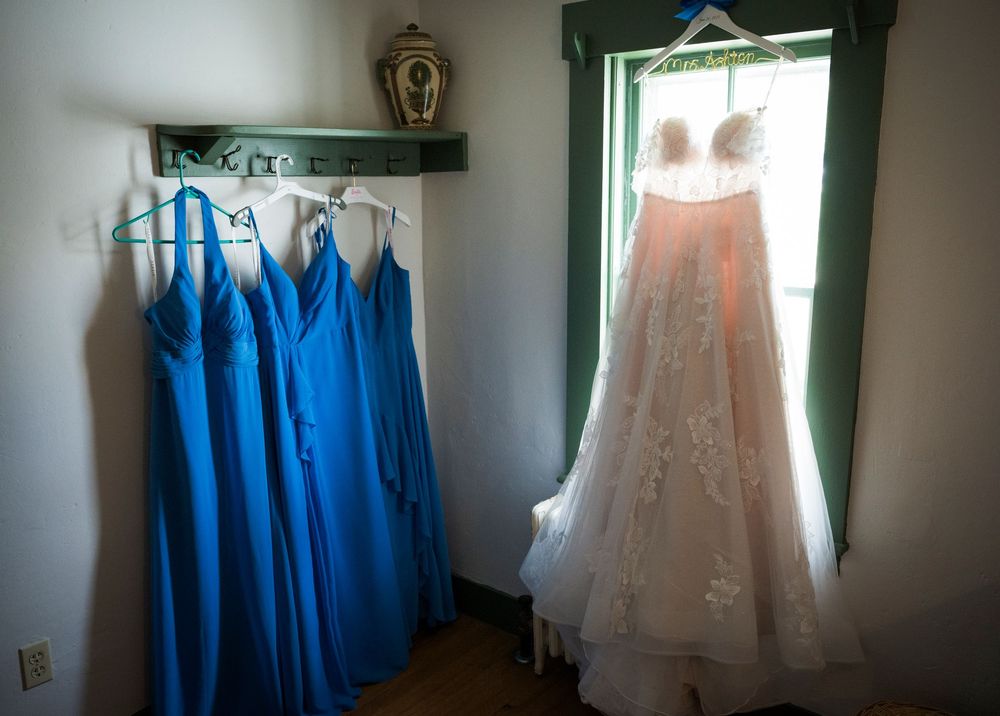 Wedding dresses and royal blue bridesmaid gowns hang on a rack against a dark wall.