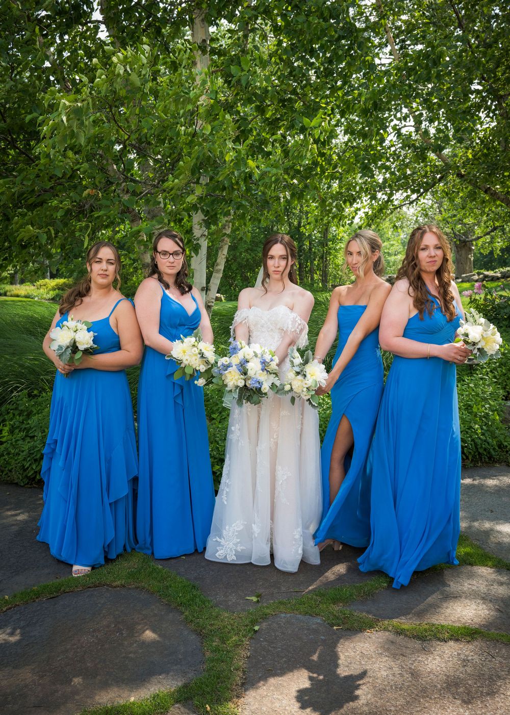 Wedding party with bridesmaids in bright blue dresses posing outdoors with bouquets.