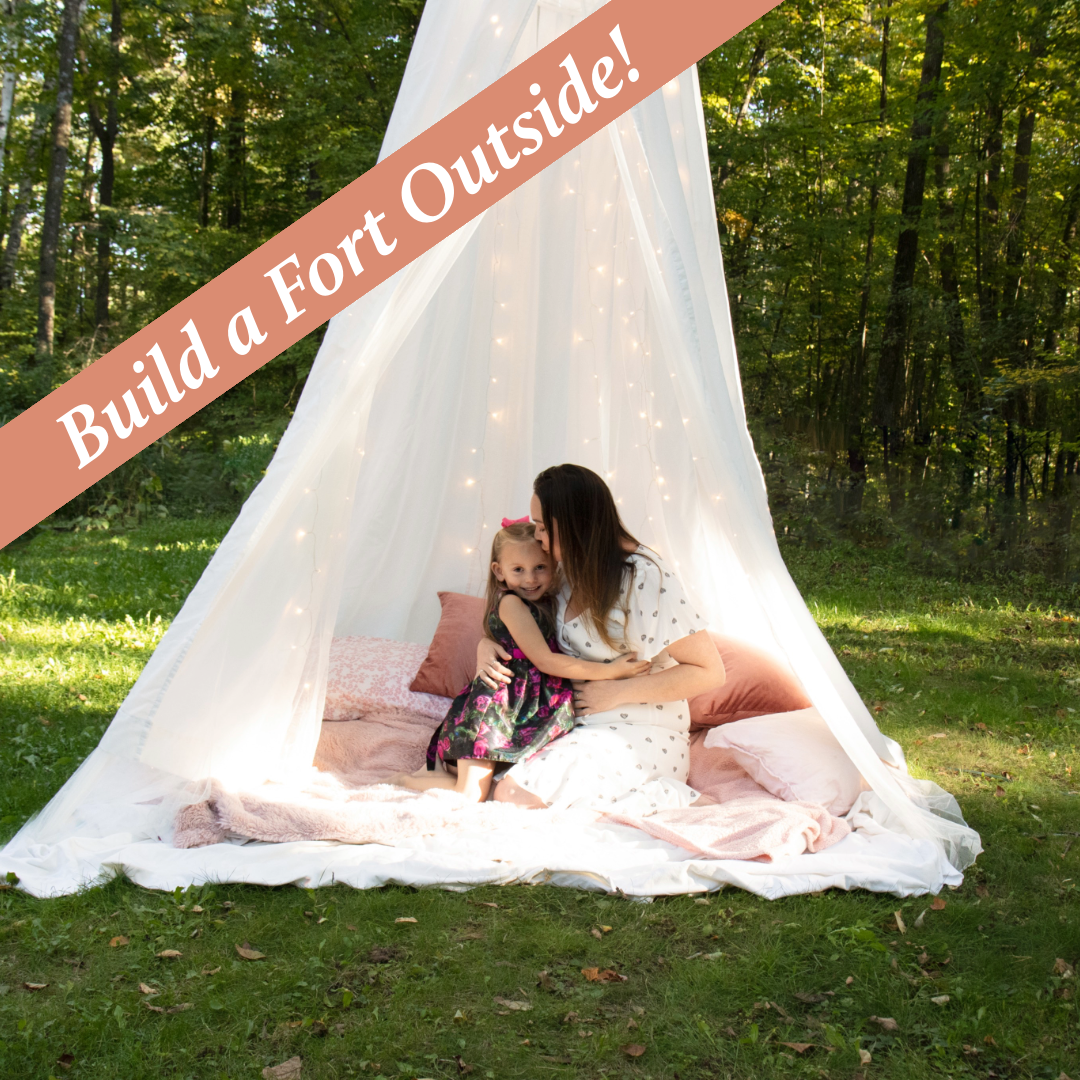 A romantic outdoor tent setting with white fabric canopy and pink accents in a wooded area during a photoshoot.