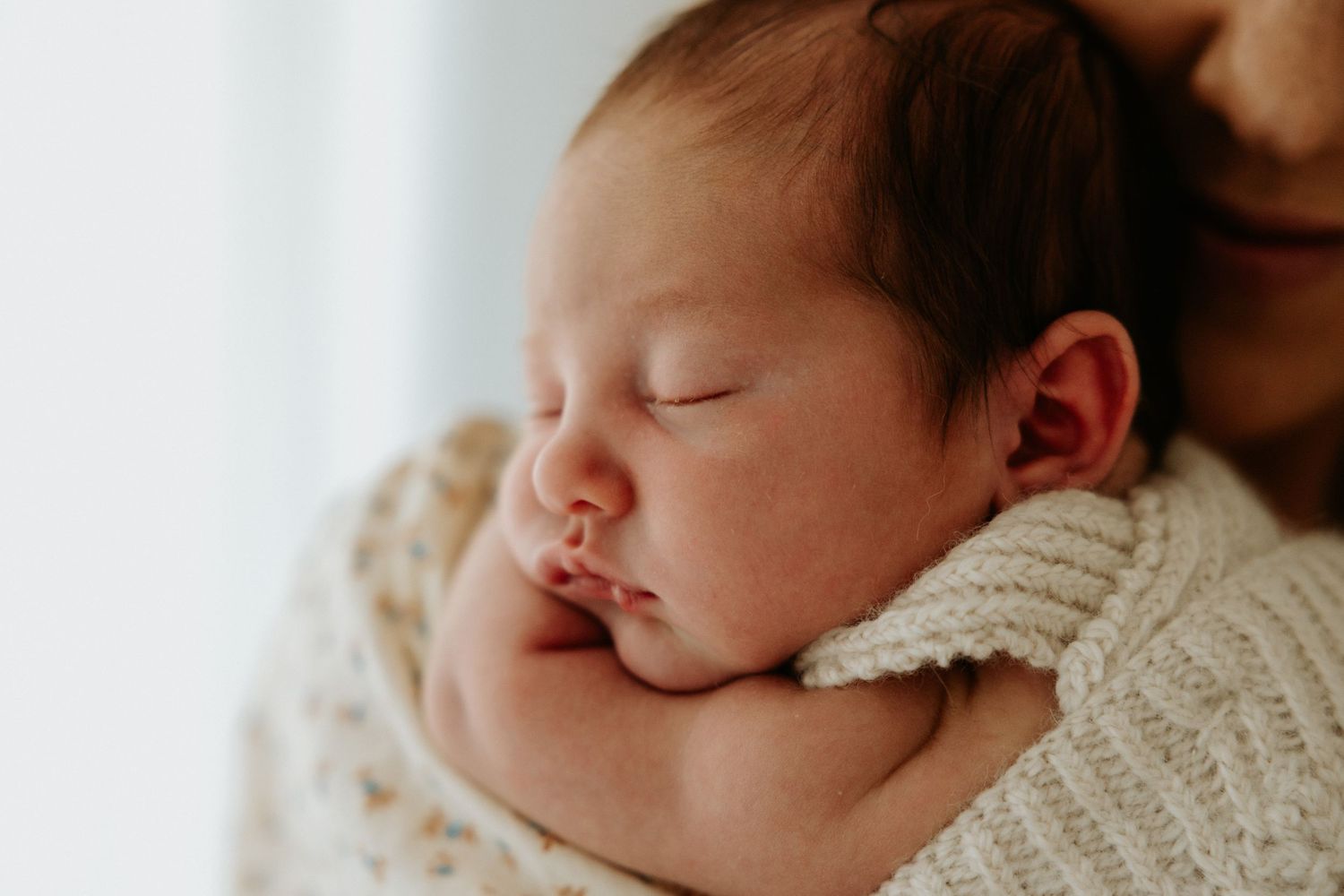 Sleeping newborn baby in soft white swaddle blanket rests peacefully during portrait session.