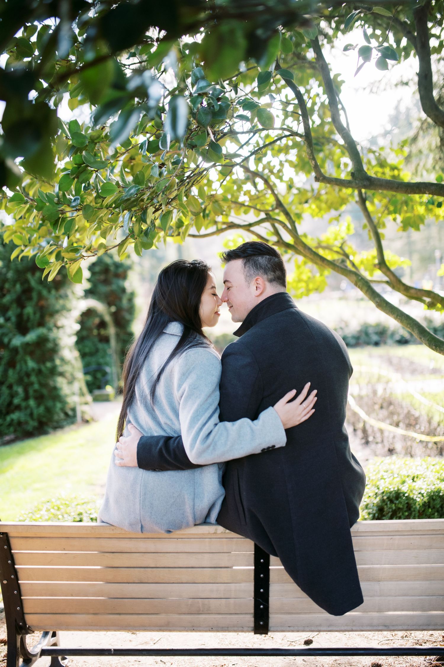 A couple sharing an intimate moment while sitting on a park bench under blooming trees.