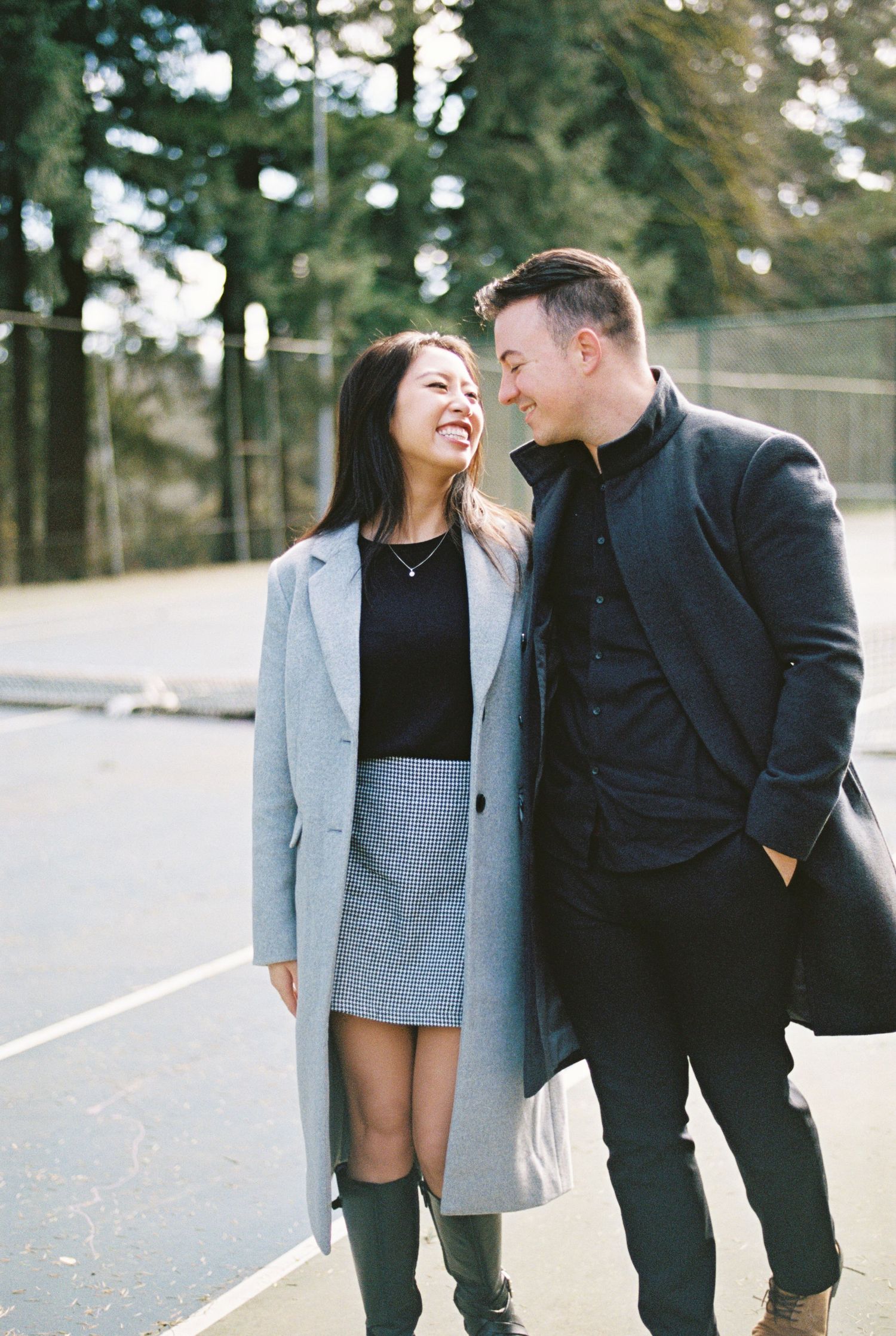 Happy couple in coordinating winter coats share a warm moment on a tree-lined path.