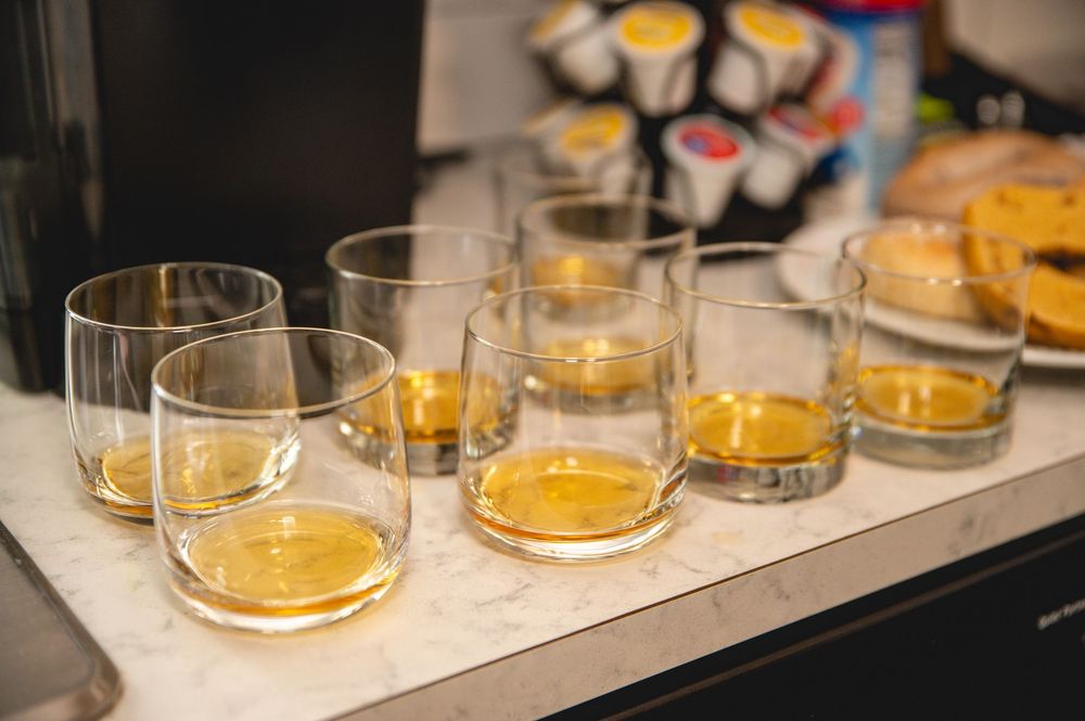 Several lowball glasses filled with amber-colored whiskey or bourbon lined up on a counter.