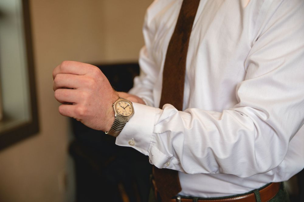 Someone in a white dress shirt fastens a watch or bracelet around their wrist.