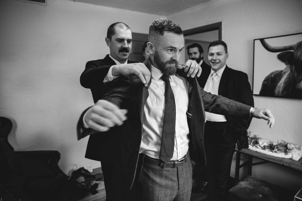 A black and white photograph shows men in suits getting dressed in what appears to be a backstage dressing room.