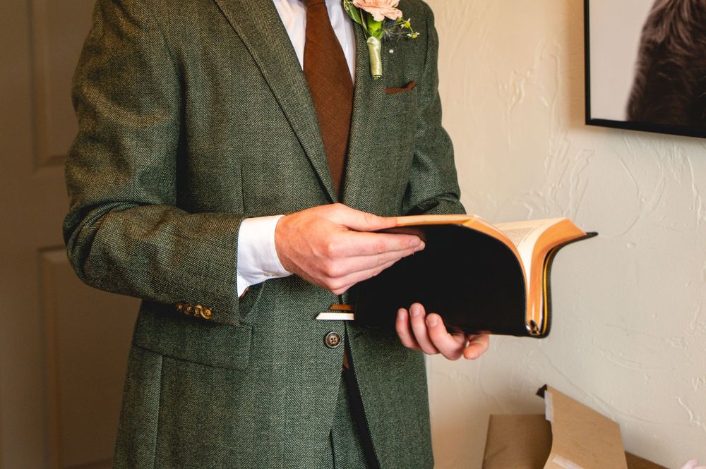 A close-up of a deep green tweed suit jacket with brown buttons and a white button-up shirt underneath.