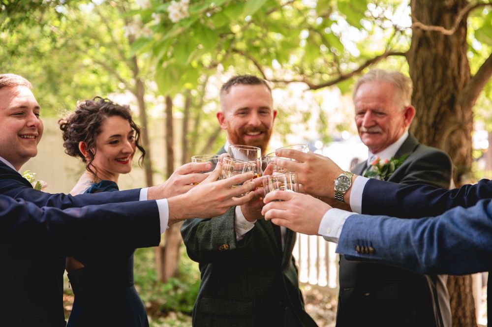 Celebratory hands with wine glasses toasting and clinking together at an outdoor gathering.