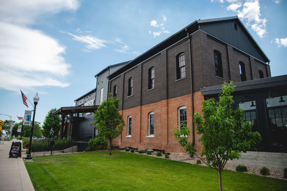 Modern brick buildings with dark roofs sit along a grassy hillside under blue skies with white clouds.