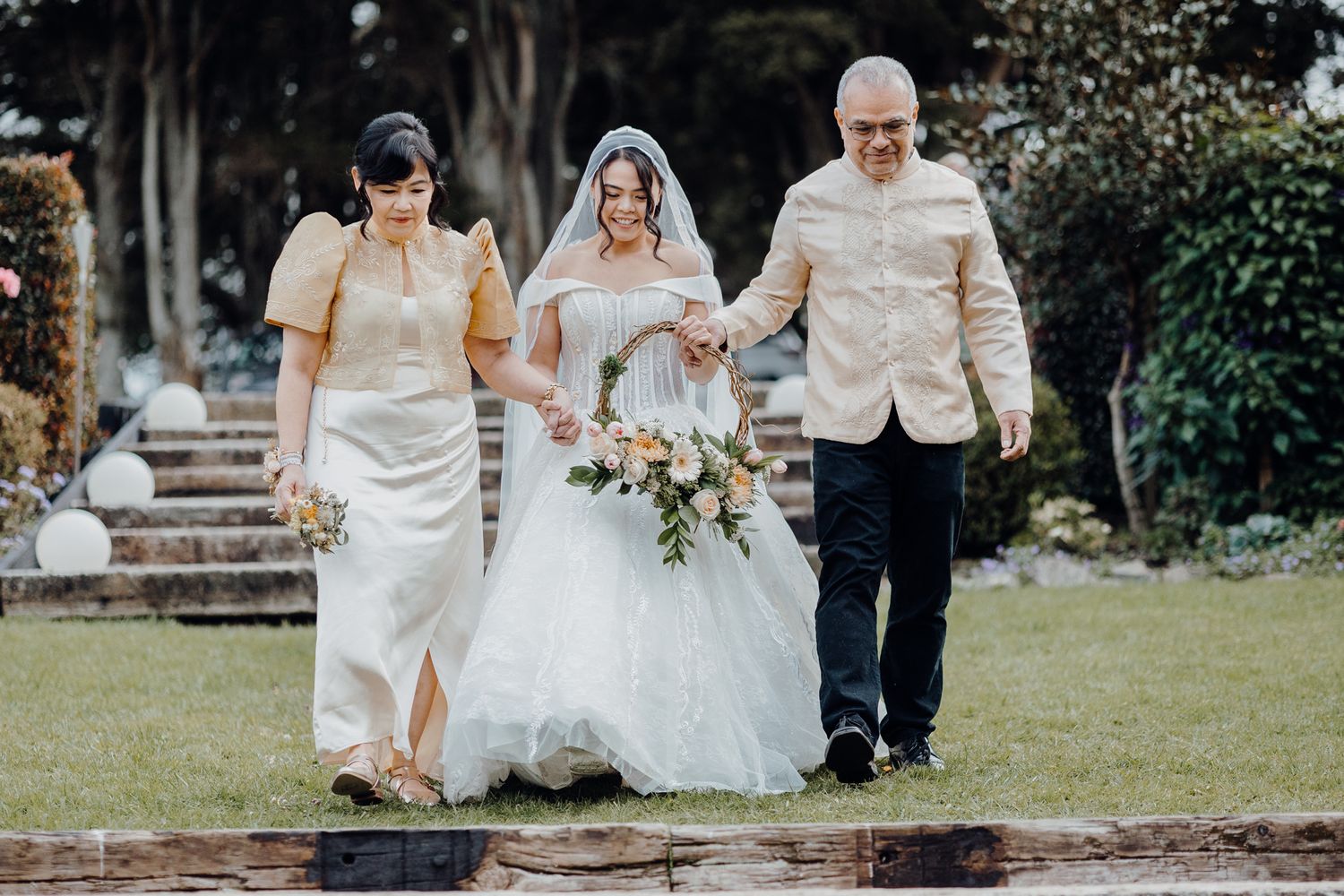 A wedding party walks down stone steps in an outdoor garden setting.