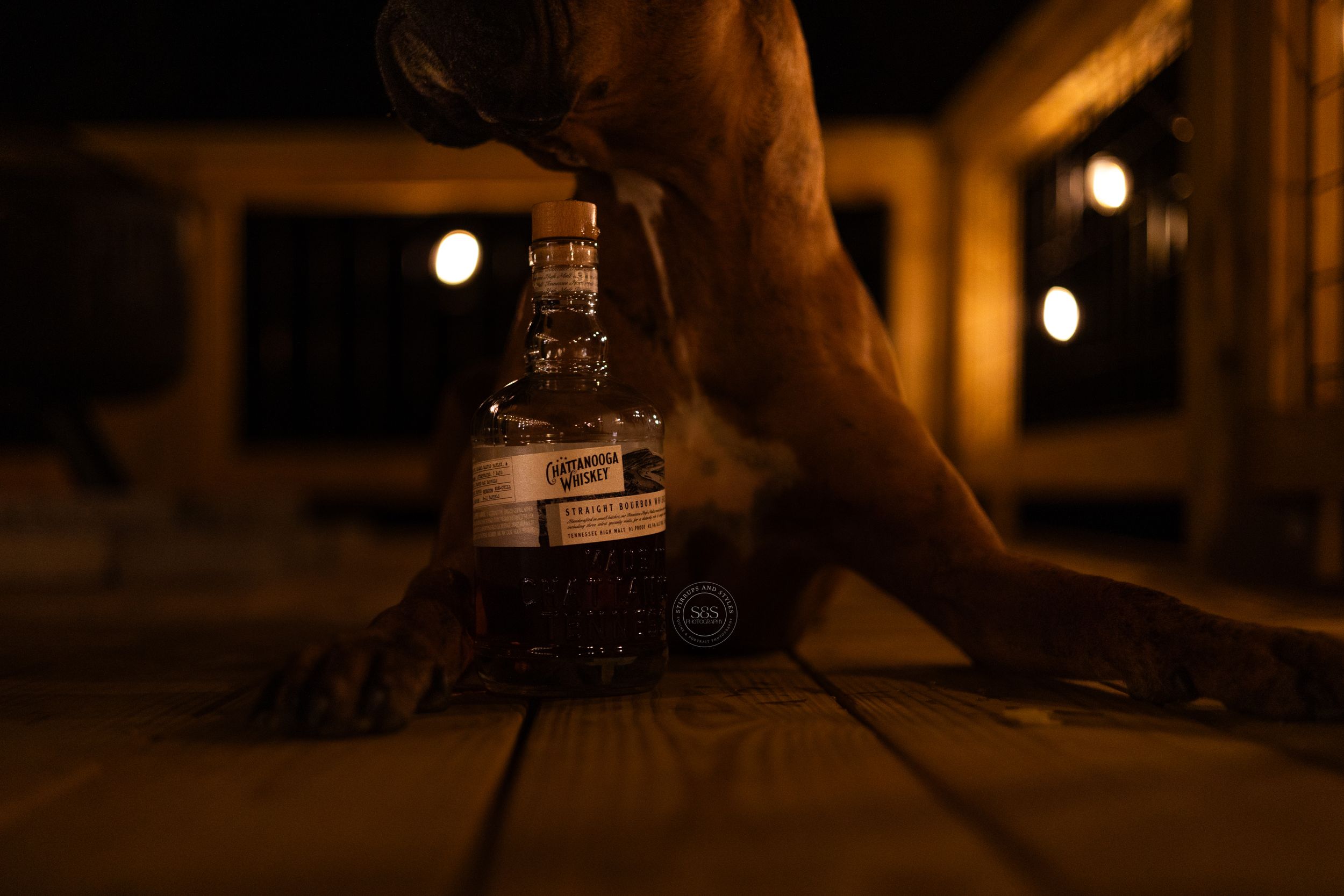 Dark moody photo of a whiskey bottle on a wooden surface at night.