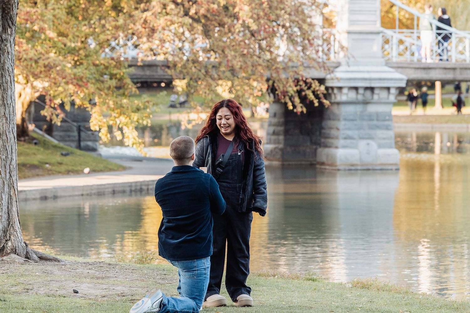 Surprise proposal moment by lake with autumn trees.