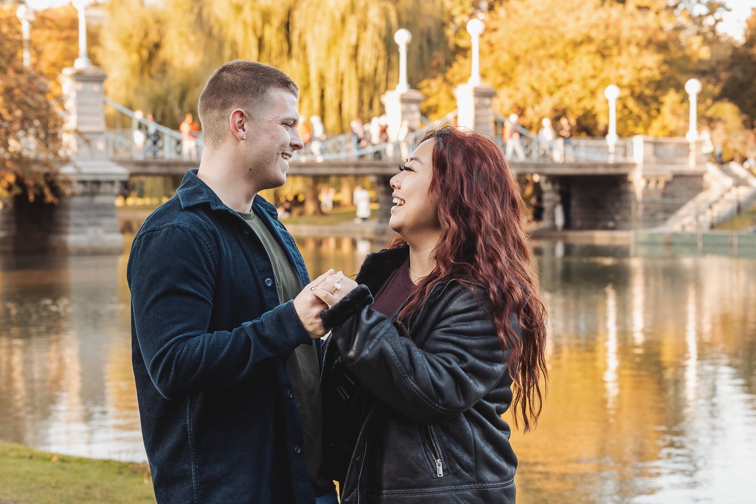 Couple sharing a joyful moment near a pond with golden willow trees and decorative stone railings.