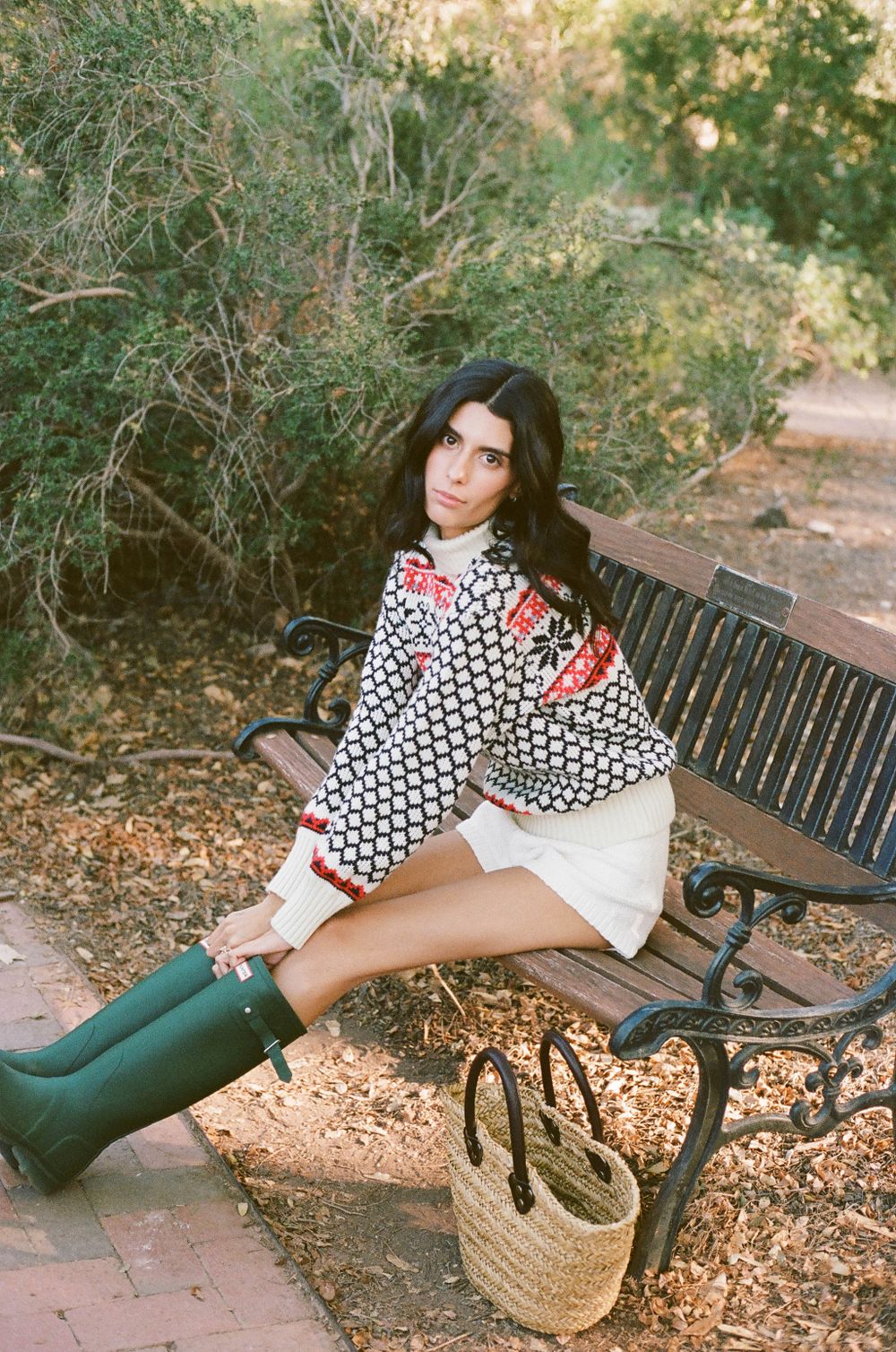 Casual outdoor portrait featuring patterned sweater, white shorts and green boots on park bench.