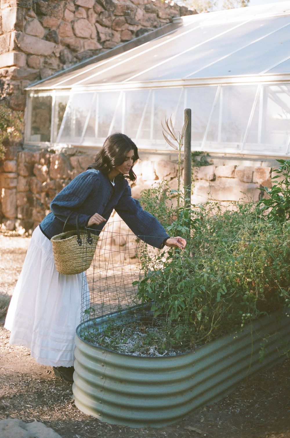 Garden scene with denim jacket and white dress reaching into raised planter bed.