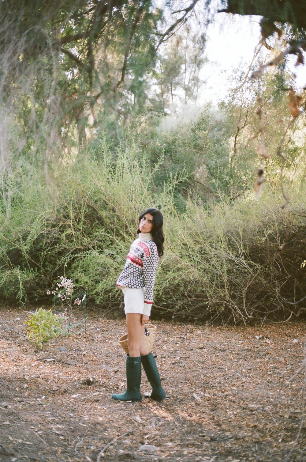 Nordic-style sweater paired with white shorts and green boots in wooded setting.