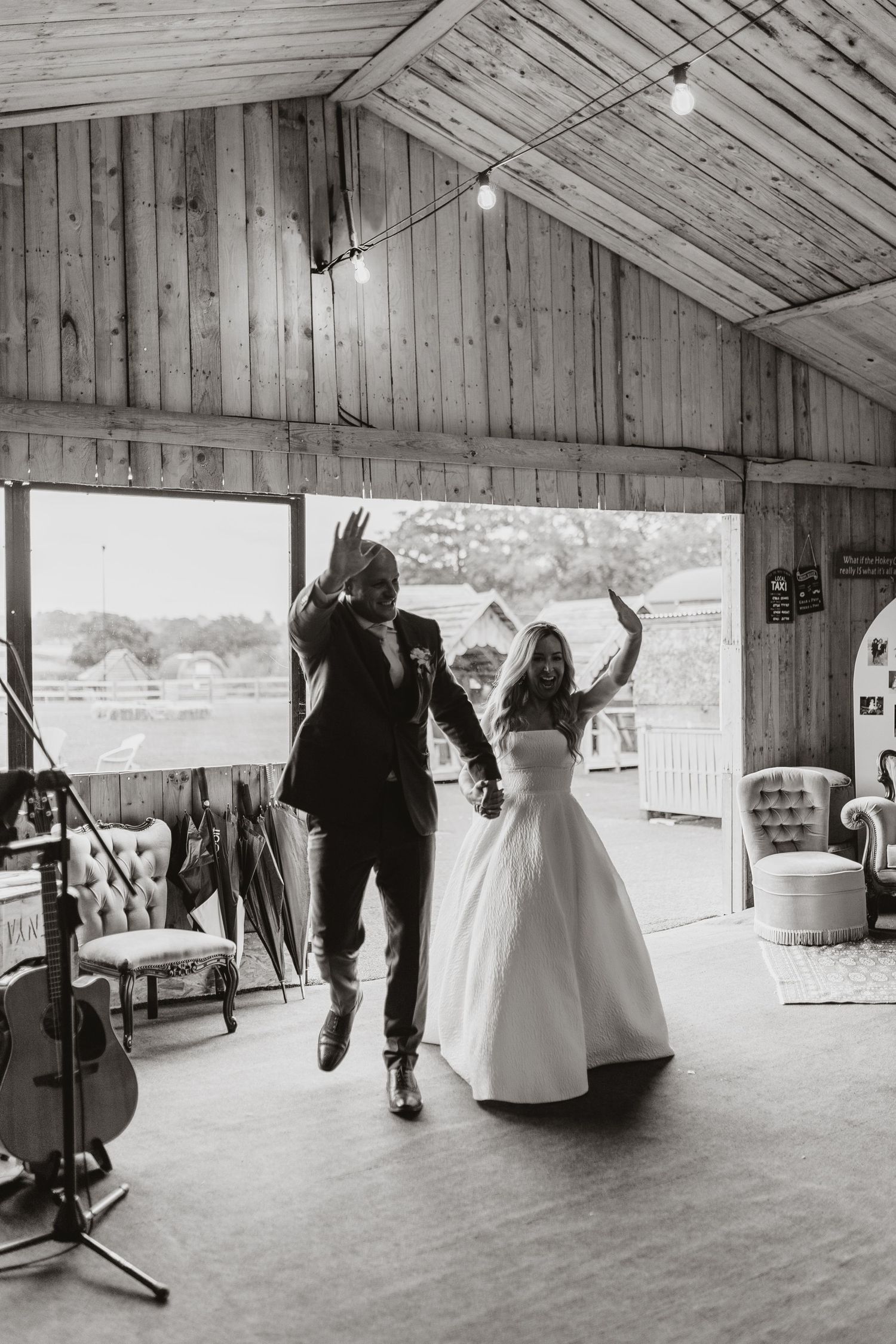 Couple dances joyfully in rustic barn venue with wooden walls and natural light streaming through doorway at Stanford Farm