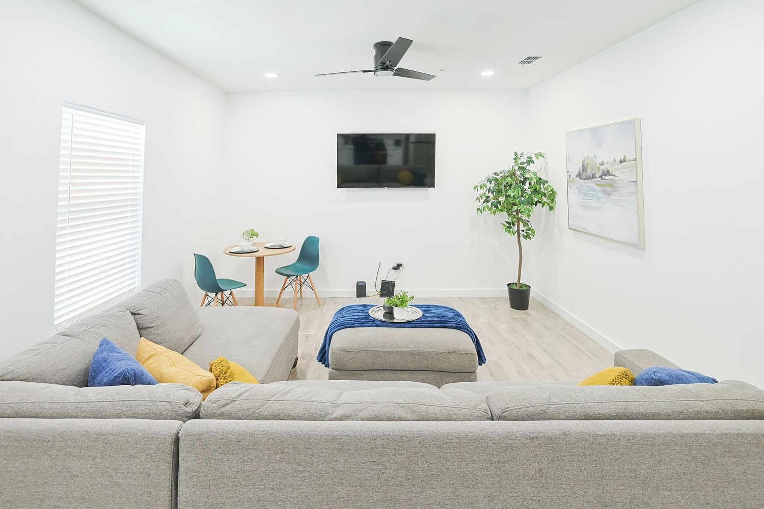 Clean white modern living room interior with bright furniture, yellow accent pillows and green potted plant.