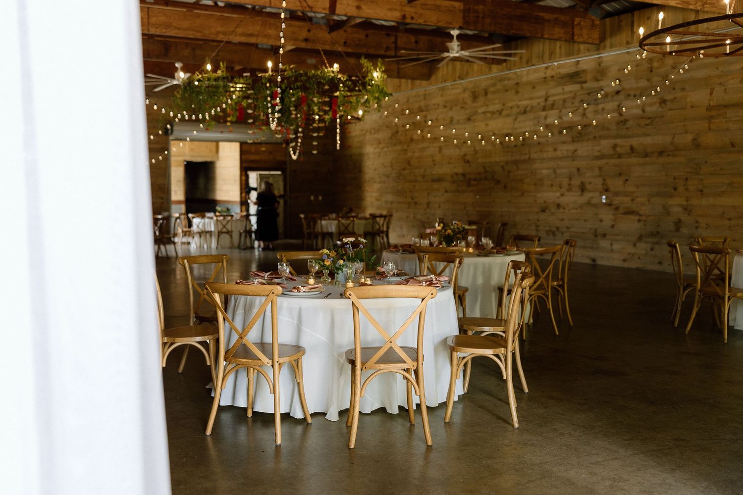 Wedding reception at Honeysuckle Hill in Asheville with rustic wood walls, string lights, and round tables with linens and gold chairs.