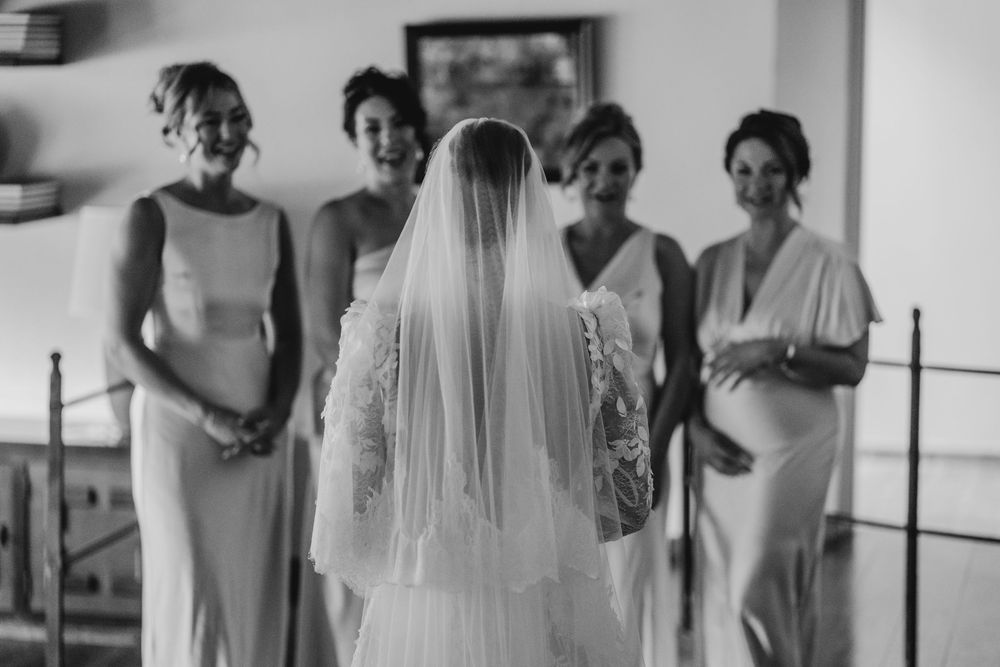 Bridesmaids share emotional reactions and smiles as they gather around the bride before a wedding ceremony.