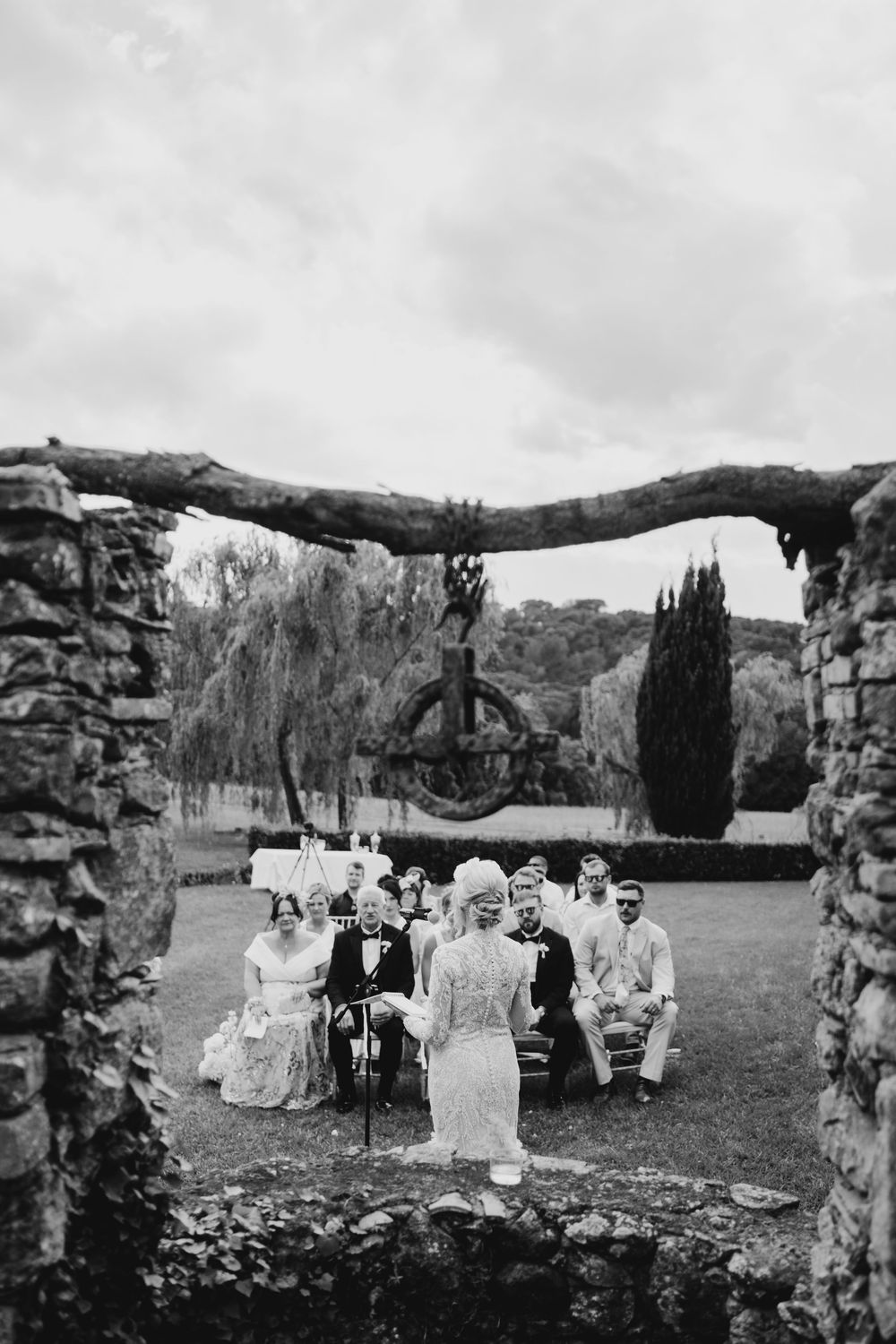 Outdoor wedding ceremony setup with white chairs arranged in rows among rolling hills and stone ruins under cloudy skies.