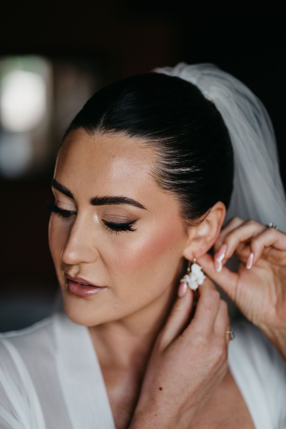 Beautiful bridal portrait showing elegant makeup and dramatic eyeliner while putting on crystal drop earrings.