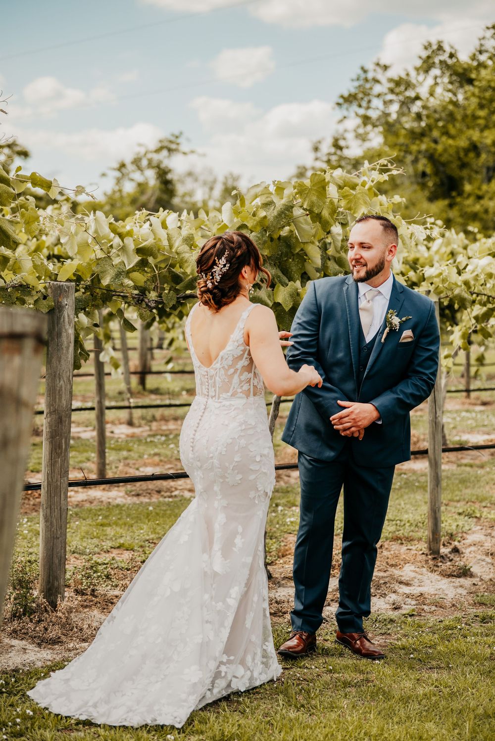 An elegant wedding photo showing a couple in formal attire sharing a moment among vineyard rows.