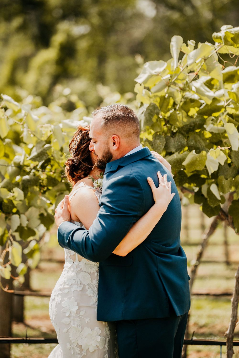 Intimate embrace between newlyweds surrounded by lush grapevines in a vineyard setting.