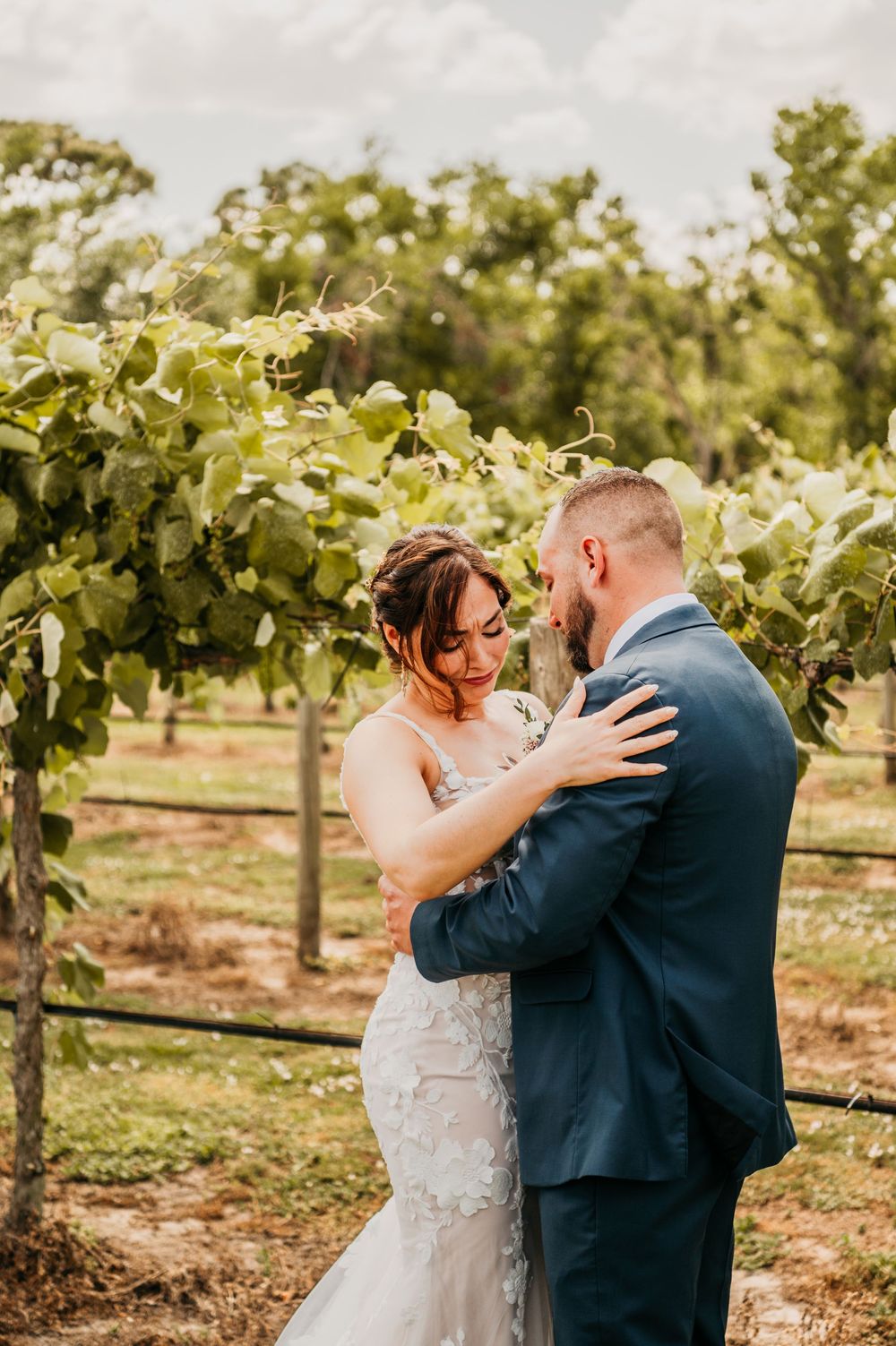 A romantic wedding moment captured in a vineyard as newlyweds embrace in formal attire.