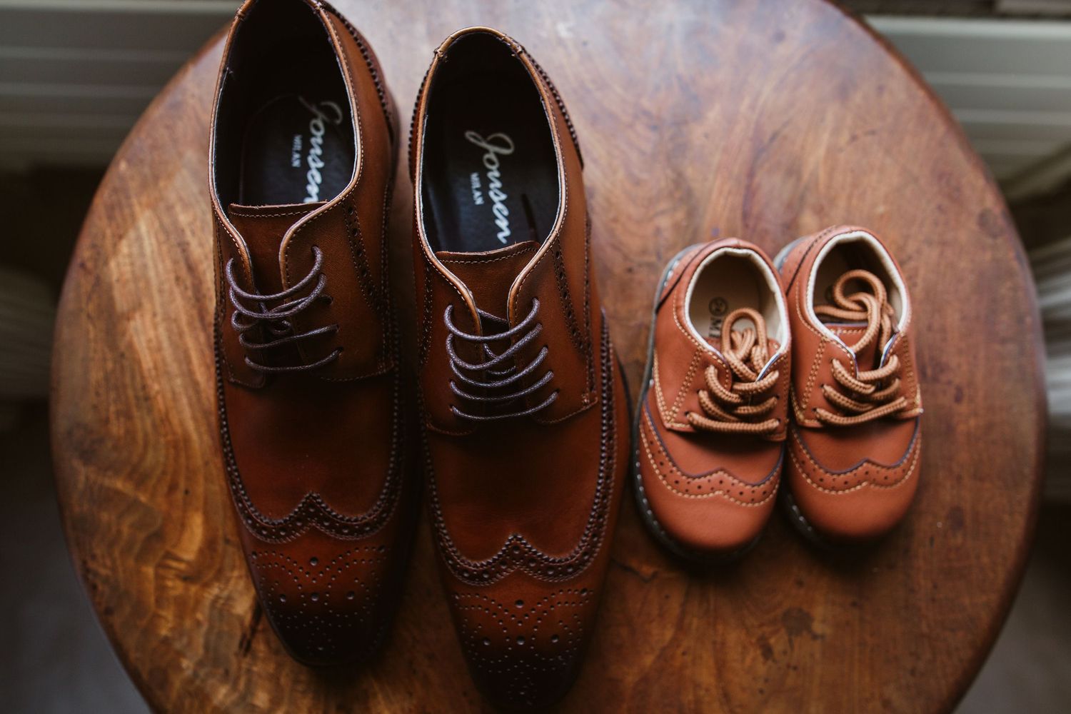 Three pairs of brown leather wingtip oxford shoes arranged on a dark wooden surface in a sliding sequence.