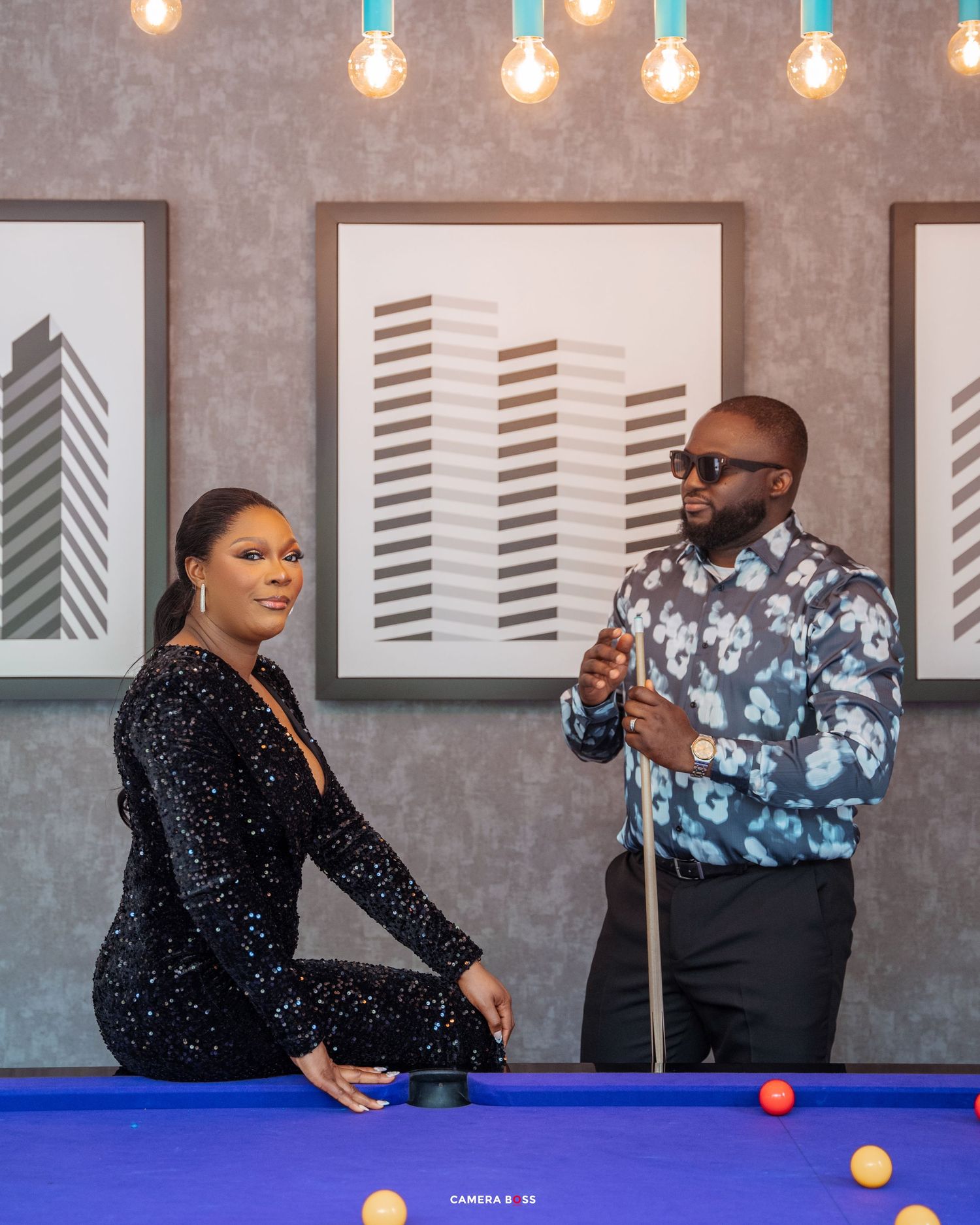 Two people enjoying a game of pool in a modern space with art prints of buildings and pendant lighting.