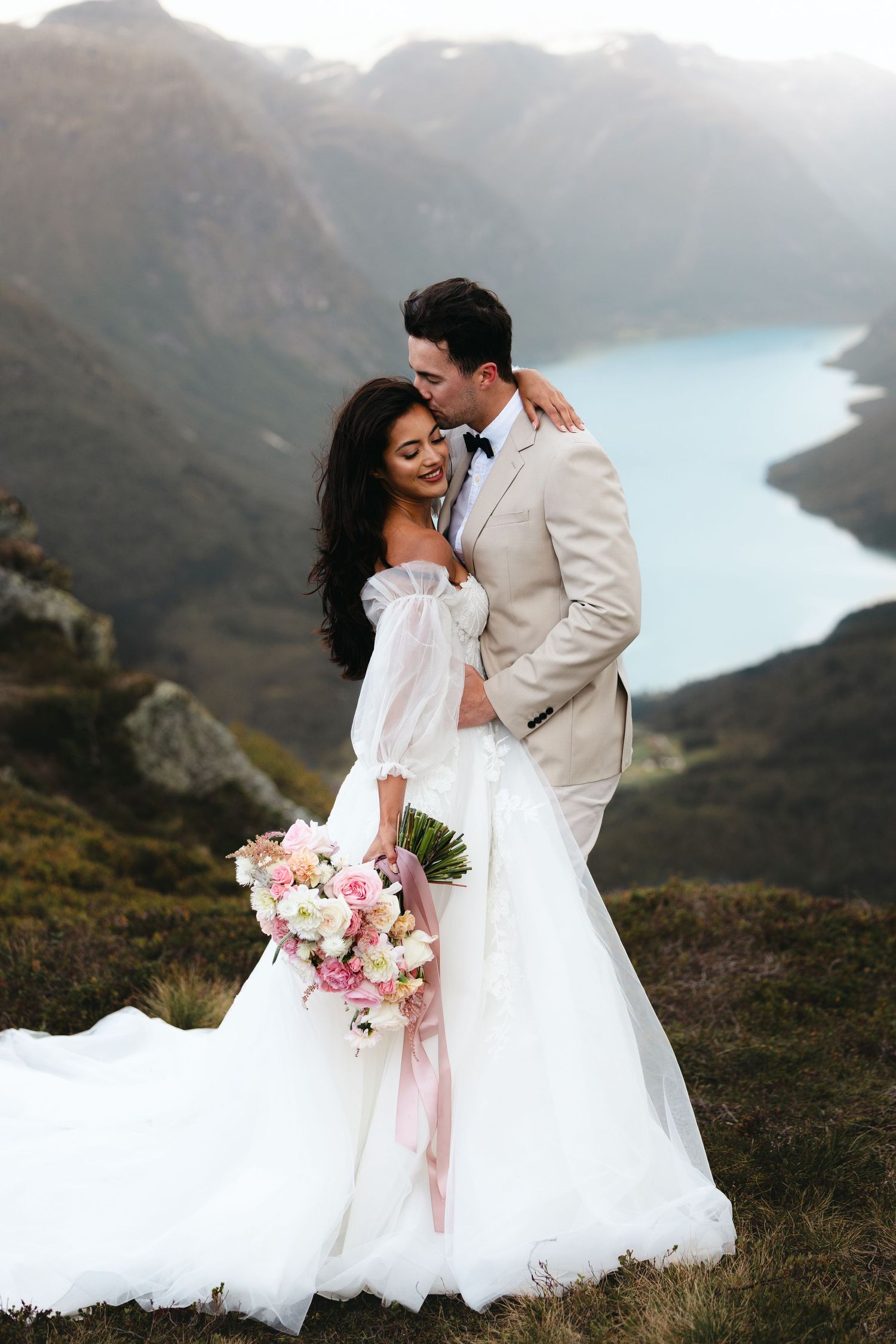 Wedding portrait with turquoise alpine lake and misty mountain vista in background.
